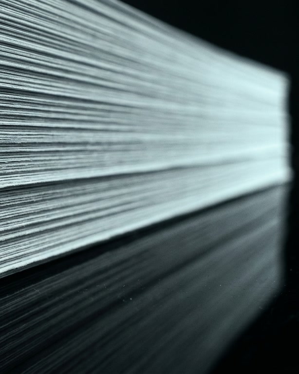 El canto de una pila de documentos perfectamente alineada, iluminado por una línea de luz fría.